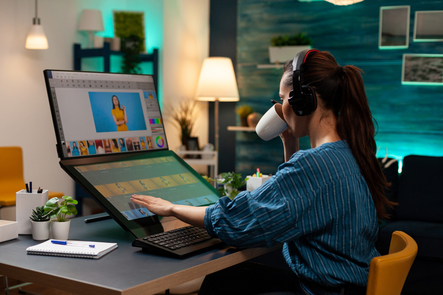 Designer gráfica com fones de ouvido revisando artes em estação de trabalho com monitor e mesa digitalizadora durante o processo de aprovação de peças de uma agência