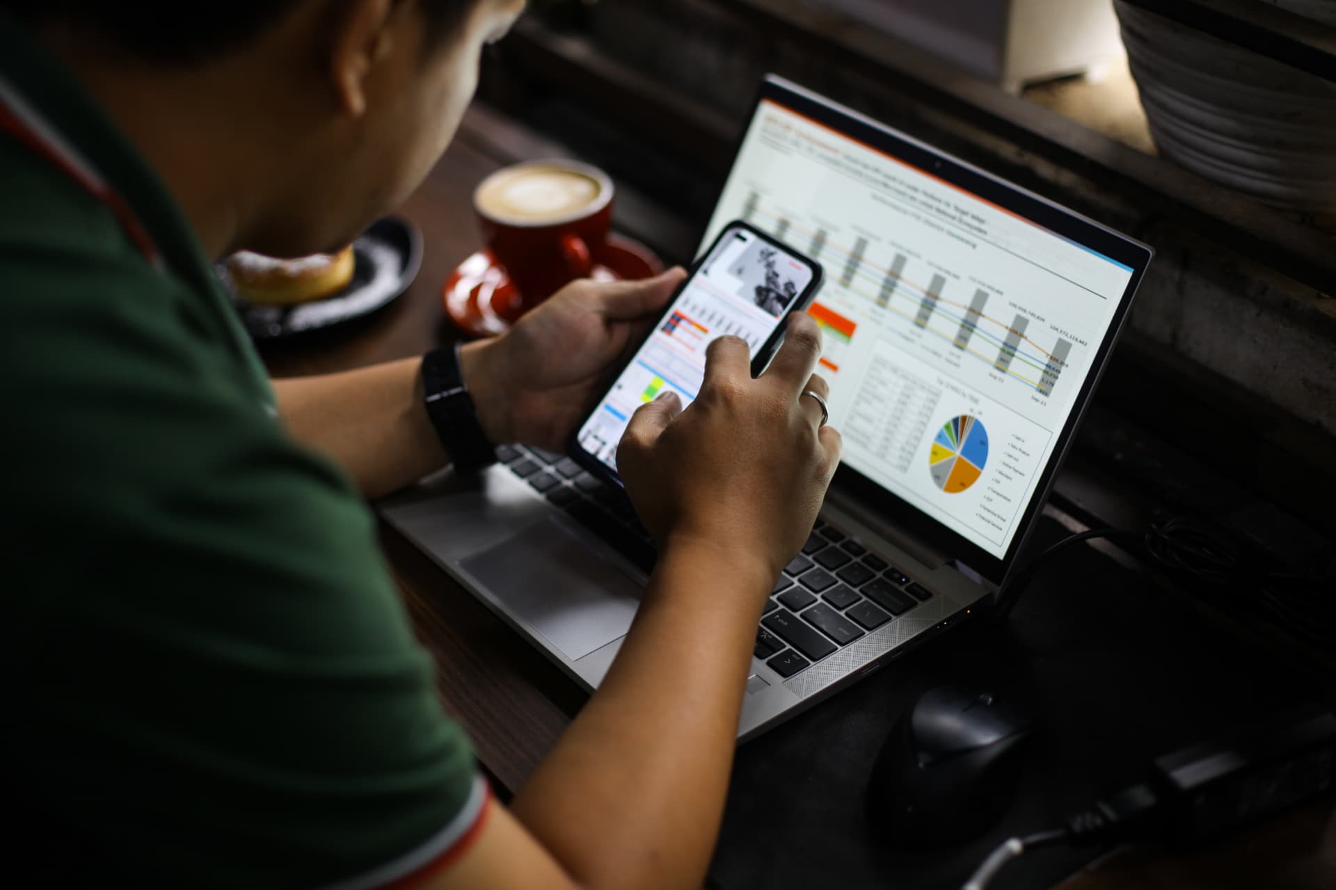 Profissional analisando gráficos e relatórios de desempenho no celular e no notebook
