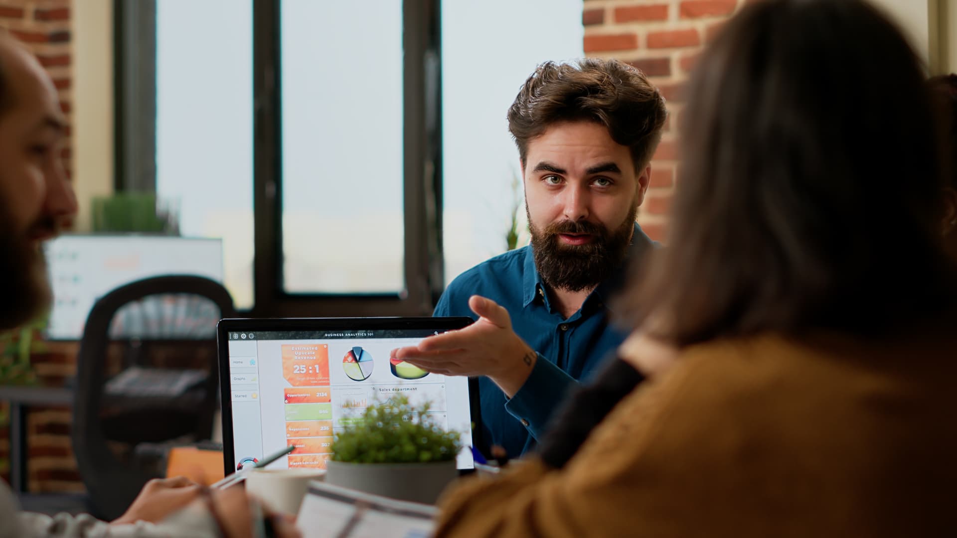 Equipe de agência reunida discutindo dados de um painel em notebook durante alinhamento de demandas