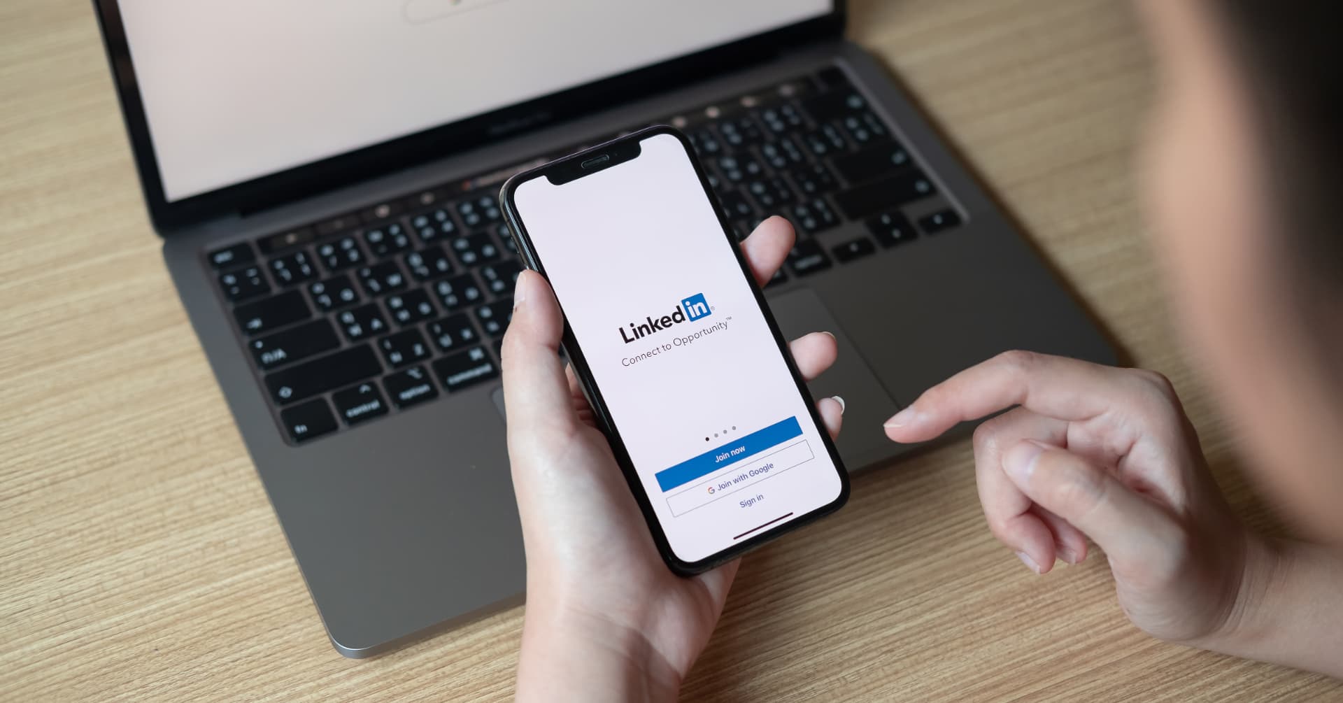 Pessoa acessando o LinkedIn no celular em frente a um notebook, ilustrando a redução de conteúdo genérico feito por IA