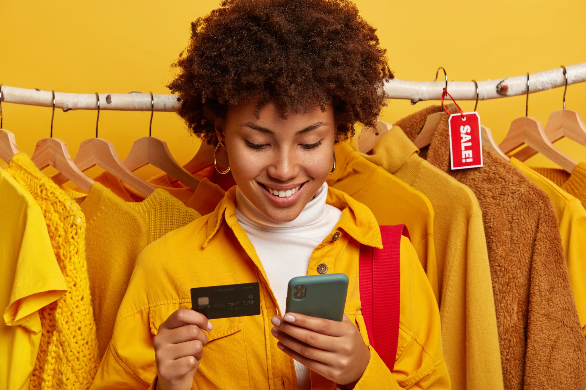 Mulher sorrindo segurando cartão e celular em uma loja de roupas, ilustrando as compras por indicação de afiliados no Instagram