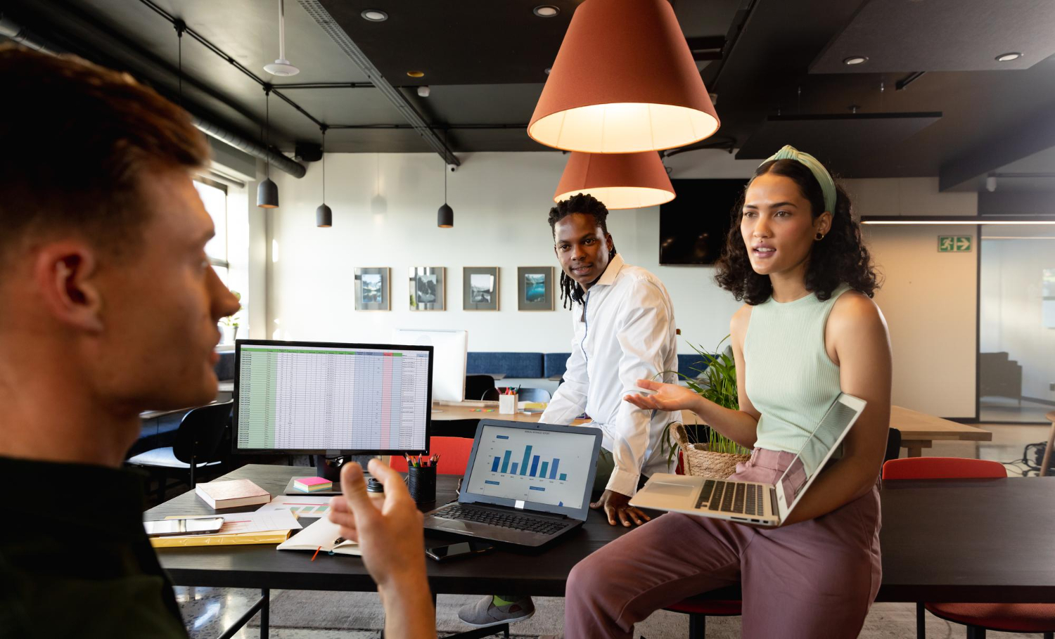 Equipe de agência de marketing reunida no escritório analisando planilhas de fluxo de trabalho e gráficos de controle de demandas em laptops