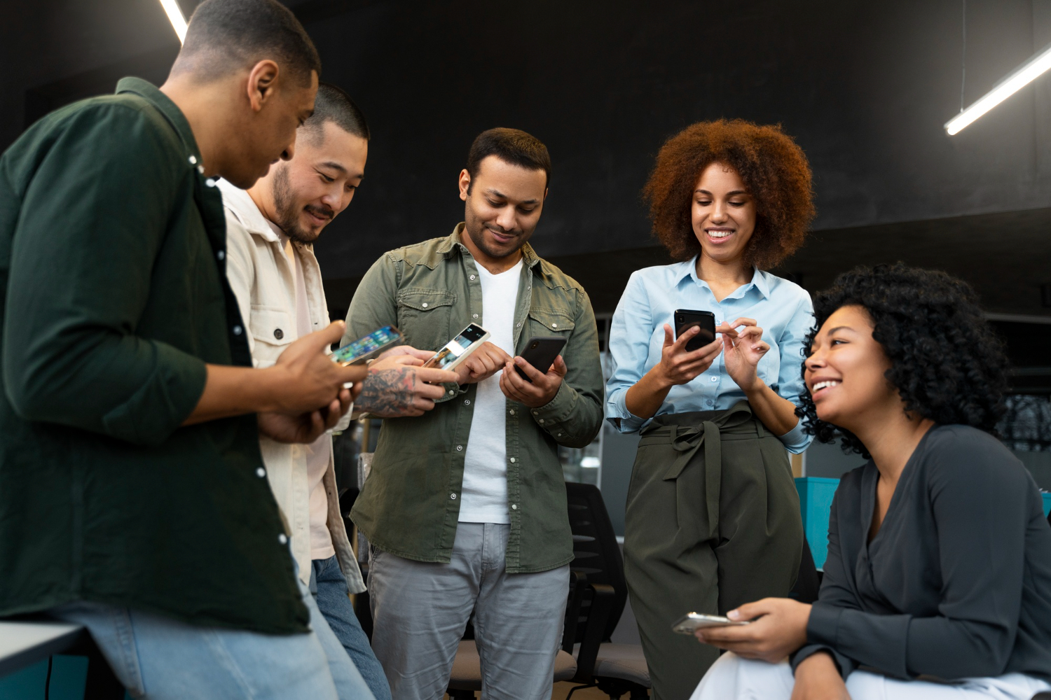 Time de agência de publicidade reunido em pé conferindo campanhas nos celulares no escritório