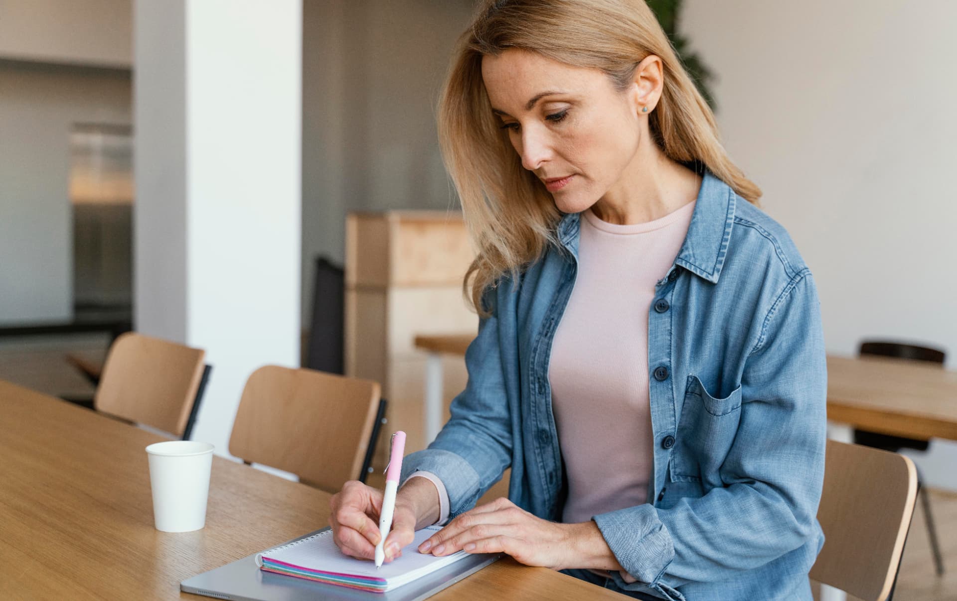 Profissional de marketing escrevendo o planejamento mensal em um caderno sobre a mesa de reunião
