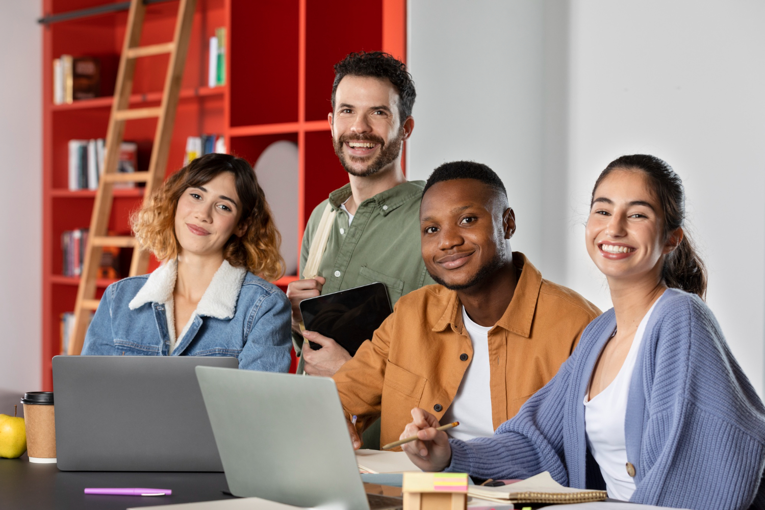 Time de uma nova agência de marketing digital sorrindo em volta da mesa com notebooks durante o planejamento do negócio